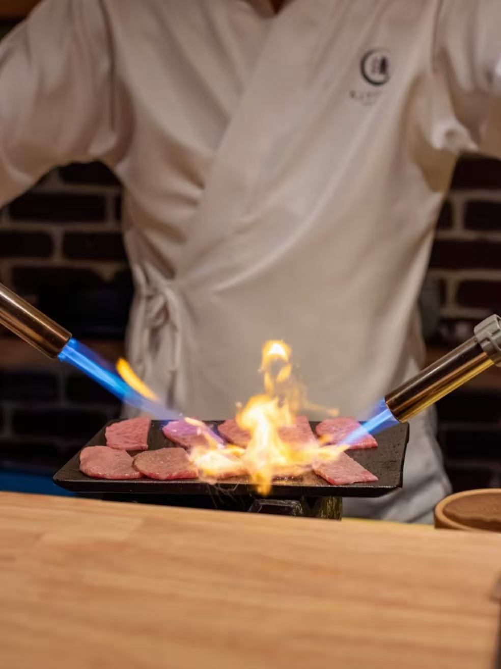 Chef using two blowtorches to sear wagyu beef during live performance at Kiyoshi Omakase